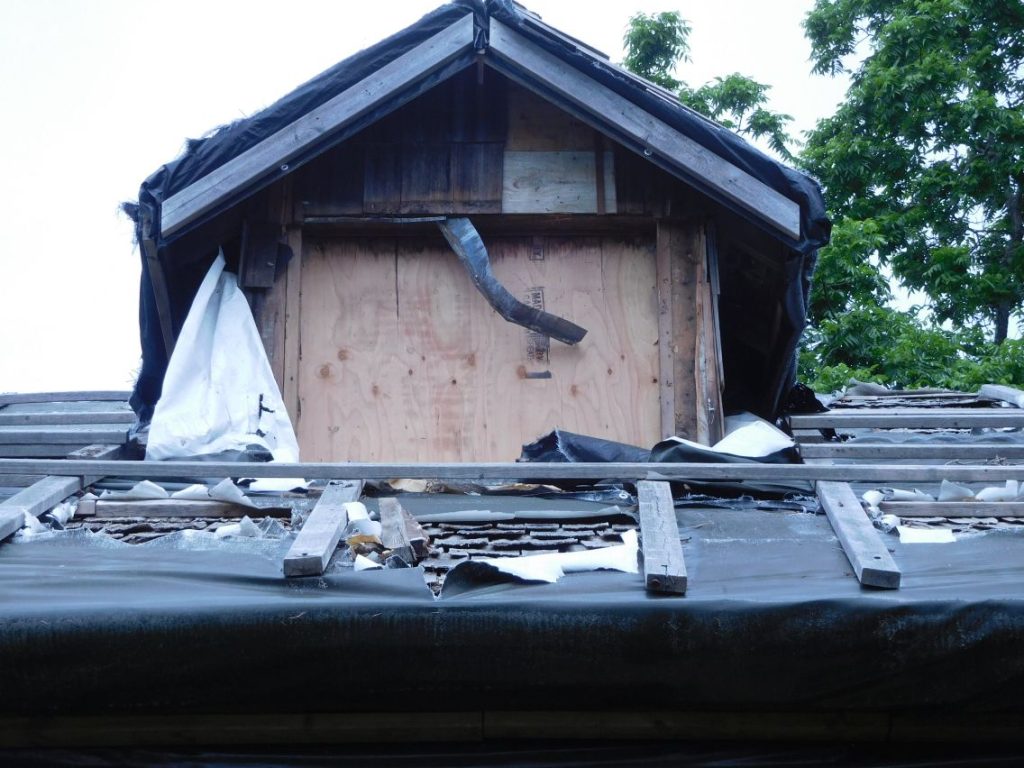 Close-up of Shakesides roof showing window frame removed from attic, and torn roof protection installed by Lacasse to prevent leakage into the house